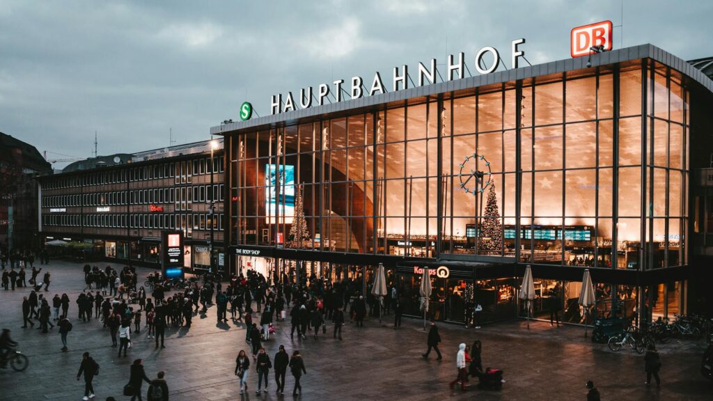 A busy train station bustling with people under the evening sky, showcasing a modern architectural design with glass walls and the sign "Hauptbahnhof" illuminated. Perfect imagery reflecting global travel and the professional services offered by the best travel agency in Lahore.